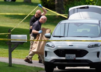 Member of law enforcement place bags of items in a vehicle at the scene of a shooting.