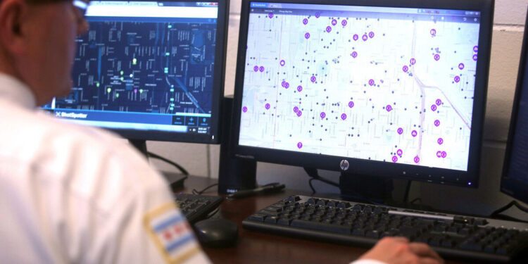A person with light skin tone, wearing a white uniform with a Chicago flag on their shoulder, looks at gunshot detection programs on two computer screens.