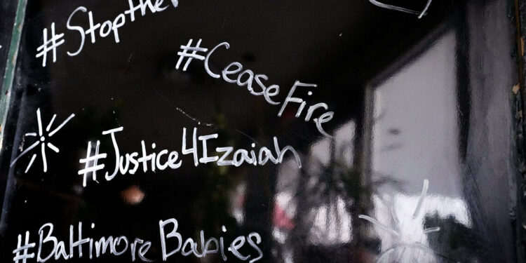 A black-colored sandwich board with messages such as “#StoptheViolence” and “BaltimoreBabies” written in white marker showing support for 16-year-old Izaiah Carter, who was shot and killed in March.