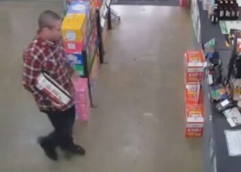 Man in red flannel carries a box of bottles inside liquor store.