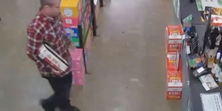Man in red flannel carries a box of bottles inside liquor store.