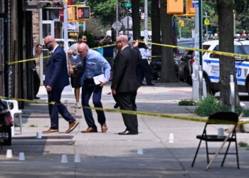 Detectives duck under crime scene tape on a sidewalk at the scene of shooting