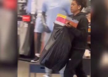 A man carrying a trash bag of shoe boxes out of a store.