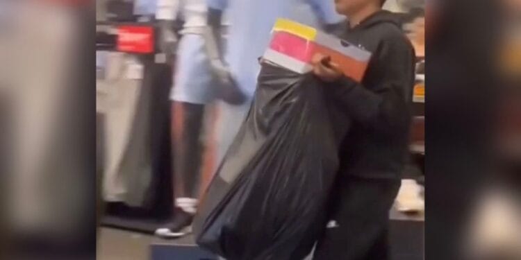 A man carrying a trash bag of shoe boxes out of a store.
