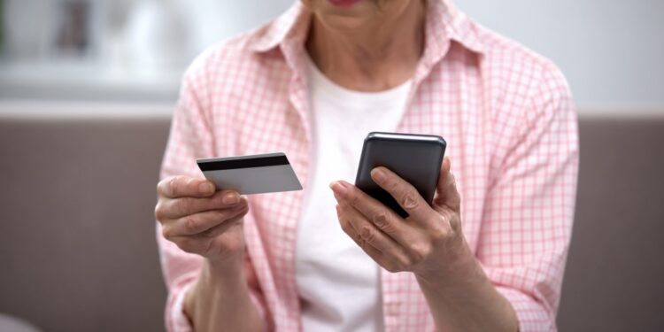 Senior female entering credit card number on smartphone.