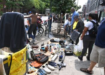 Crowd of people gathered around spread of wares being sold by illegal street vendors