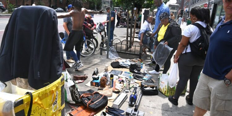 Crowd of people gathered around spread of wares being sold by illegal street vendors
