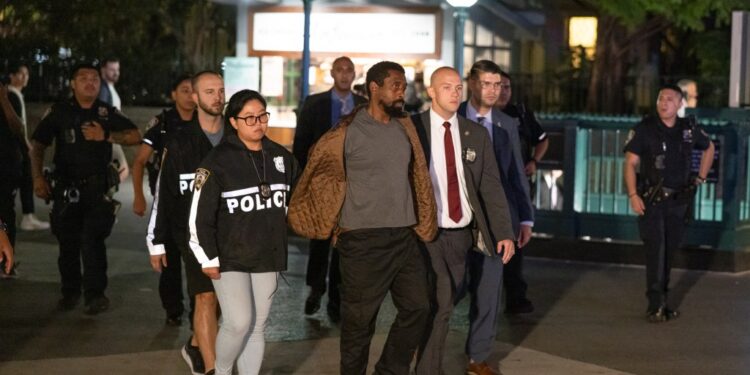 Derrick Mills in handcuffs is escorted by police officers near a subway station.