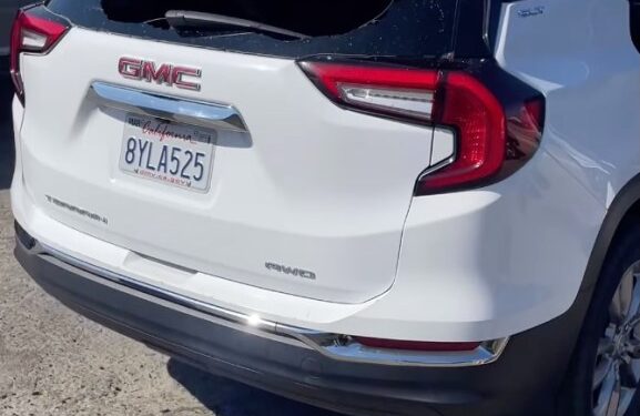A white GMC SUV is pictured with the back windshield shattered and glass strewn on the ground.