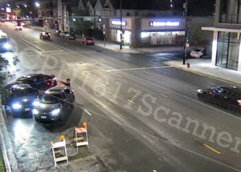An armed man is seen approaching the Audi, which is trapped between two vehicles.