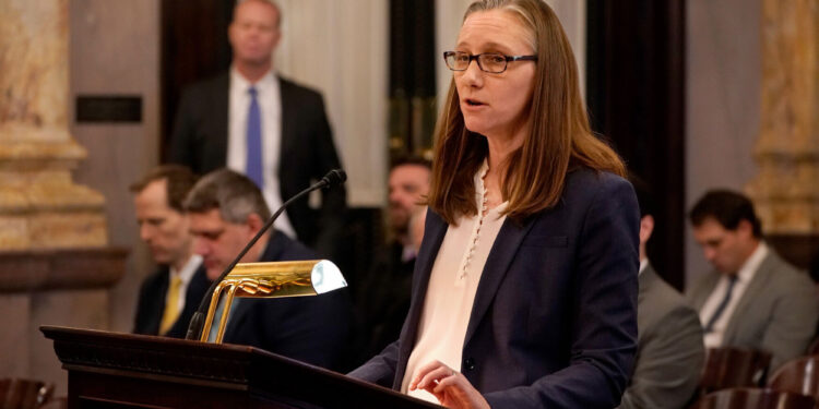 A White woman with glasses speaks at a podium.