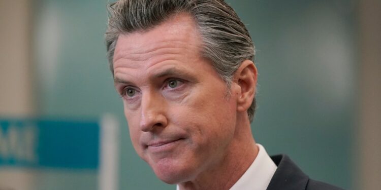 Governor Gavin Newsom speaking at a news conference, with a blurred background of an audience.