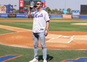 Jonathan Wibben singing into a microphone on a baseball field.