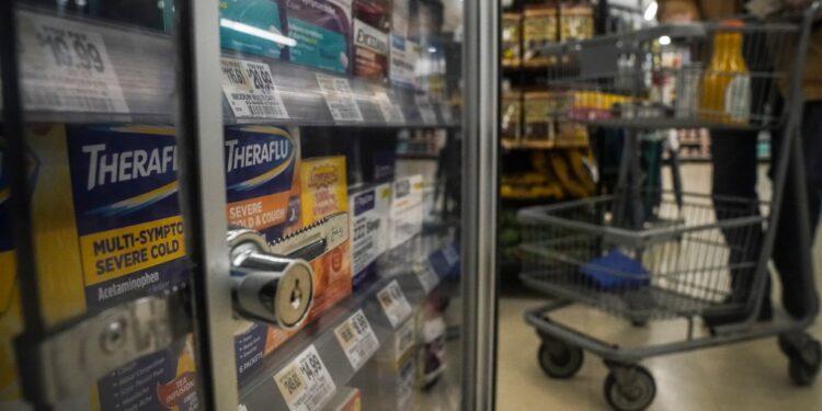 Locked pharmaceuticals in a glass cabinet at a store with a shopping cart visible in the background.