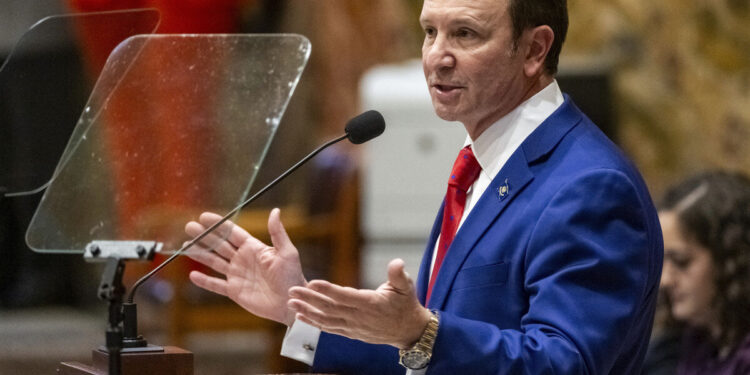 Gov. Jeff Landry, a White man wearing a blue suit and red tie, speaking at a podium in January 2024.