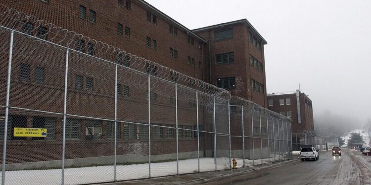 A red brick correctional facility behind a barbed wire fence.