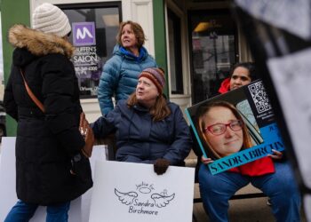 Four people at a protest for Sandra Birchmore, including Sandra's second cousin, Barbara Wright, a White woman with long brown hair, near Stoughton Town Hall. Two people hold signs saying "Justice for Sandra Birchmore."