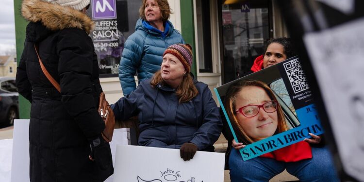 Four people at a protest for Sandra Birchmore, including Sandra's second cousin, Barbara Wright, a White woman with long brown hair, near Stoughton Town Hall. Two people hold signs saying "Justice for Sandra Birchmore."