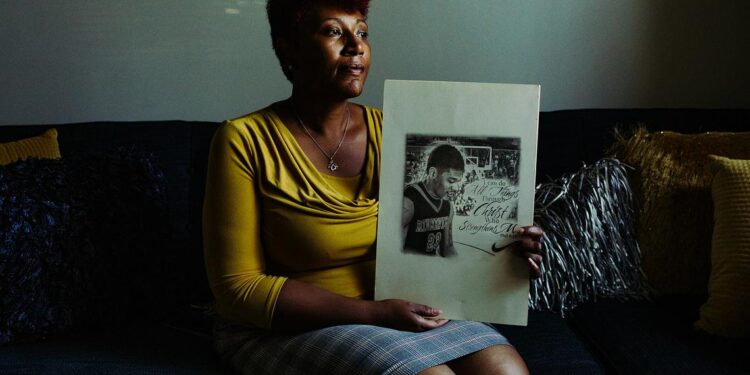 A woman wearing a yellow top and holding a drawing of her son playing basketball.
