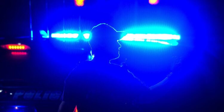 Traffic lights highlight the silhouette of a police officer as they wave their arm.