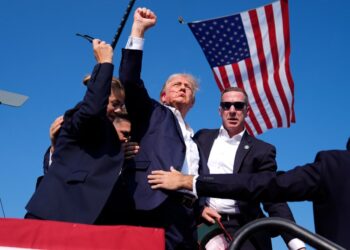 Former President Donald Trump, surrounded by U.S. Secret Service agents, gesturing as he leaves the stage at a campaign rally in Butler, Pa, in 2024