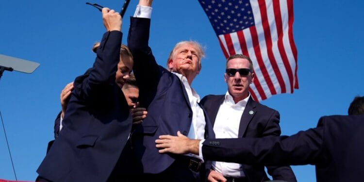 Former President Donald Trump, surrounded by U.S. Secret Service agents, gesturing as he leaves the stage at a campaign rally in Butler, Pa, in 2024