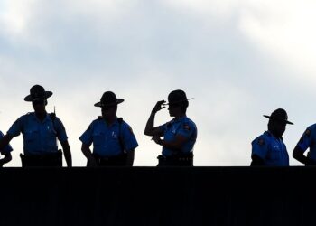 An image shows the silhouettes of six police officers standing on a bridge against a cloudy background.