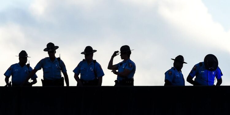 An image shows the silhouettes of six police officers standing on a bridge against a cloudy background.