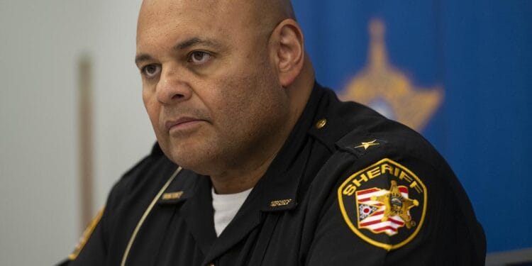 Cuyahoga County Sheriff Harold Pretel, a bald man with medium-toned skin, wears a black uniform with a sheriff’s patch on his left shoulder.