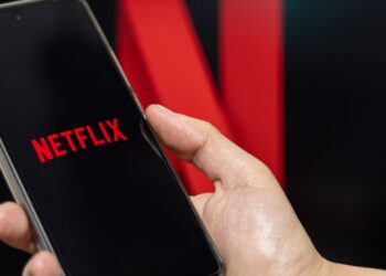 A person opening Netflix on their phone with the Netflix photo in the background.