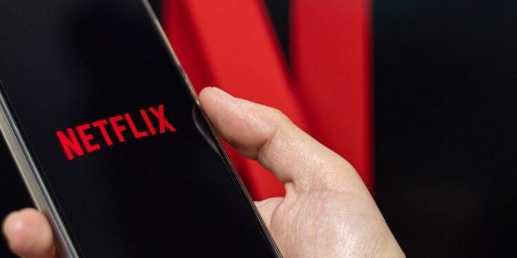 A person opening Netflix on their phone with the Netflix photo in the background.