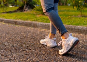 Young woman exercising by walking on a brown street, wearing white shoes