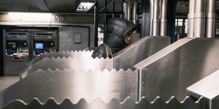 Commuters passing by a serrated metal siding installed on turnstiles at the 59th Street/Lexington Avenue subway station to prevent fare evasion