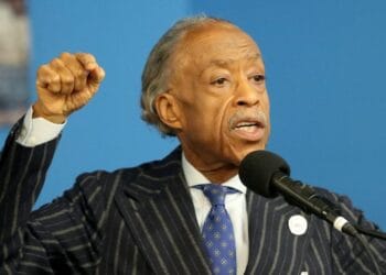 Rev. Al Sharpton in a suit speaking at the National Action Network in Harlem, holding up his fist