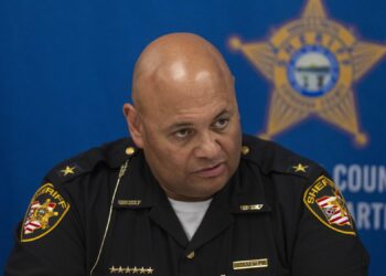 Sheriff Harold Pretel, a man with medium-toned skin, wearing a sheriff's uniform, sits in front of a blue background with a sheriff's star printed on it.