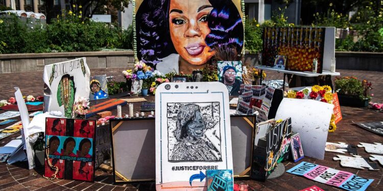 A photo shows a memorial for Breonna Taylor, with flowers, artwork and illustrations of a Black woman with shoulder-length hair.