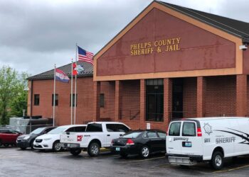 A photo of an orange brick building with a sign that reads “Phelps County Sheriff and Jail.” Several cars are parked in front of the building.