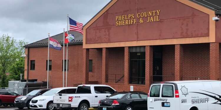 A photo of an orange brick building with a sign that reads “Phelps County Sheriff and Jail.” Several cars are parked in front of the building.
