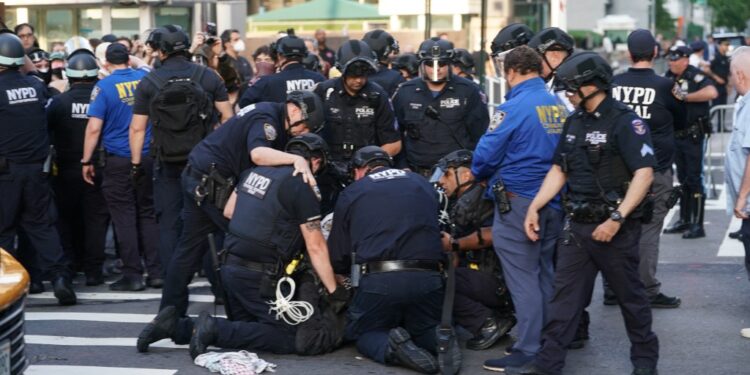 NYPD officers detaining a demonstrator at an ICE protest.