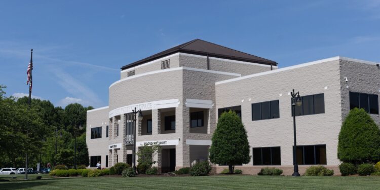 A photo of a beige, two-story building with a green lawn, under a blue sky with a few clouds.