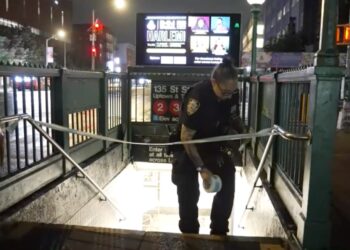 Police officer securing a subway entrance with police tape.