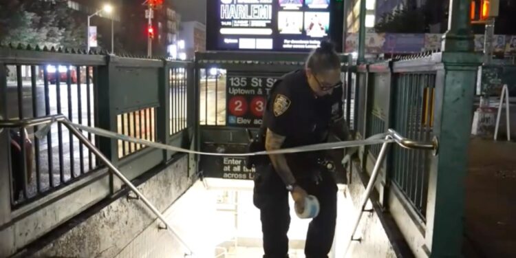 Police officer securing a subway entrance with police tape.