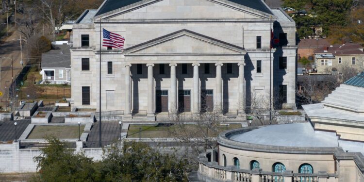 An aerial photograph of the Mississippi Supreme Court building, a beige, multi-story building with a pointed roof and columns.