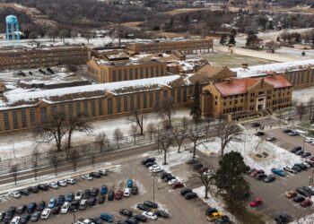 An aerial view of a tan brick prison facility with cars parked in front.