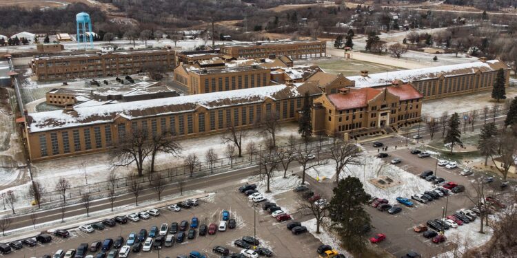 An aerial view of a tan brick prison facility with cars parked in front.