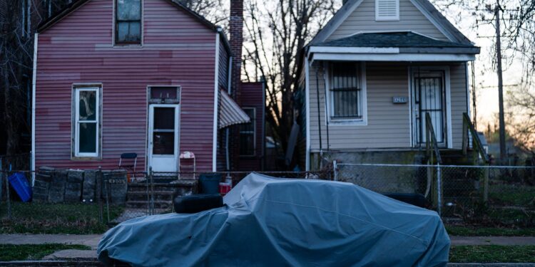 A photo shows a tarp-covered car parked on a street in front of a red house and a tan house.