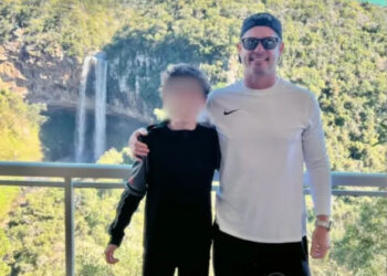 Father and son standing on balcony overlooking waterfall.  Son's face is blurred.