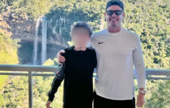Father and son standing on balcony overlooking waterfall.  Son's face is blurred.