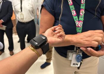 A photo shows a black electronic device attached to the wrist of a person with medium skin tone.