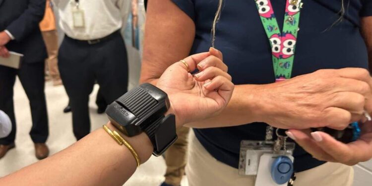 A photo shows a black electronic device attached to the wrist of a person with medium skin tone.